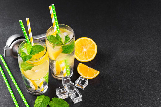 Top view of refreshing cold icy beverage, homemade lemonade with fresh lemon slices, mint leaves, ice cubes wtih soda water and condensation in glasses on black background with copy space for text.