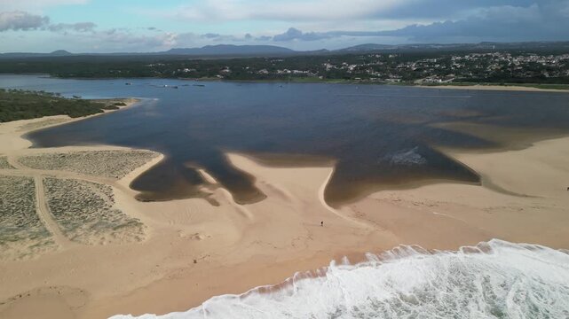 Aerial view of the sandy beach and calm waters of Praia da Lagoa de Albufeira-Mar with distant coastal town buildings in Sesimbra, Setubal, Portugal.