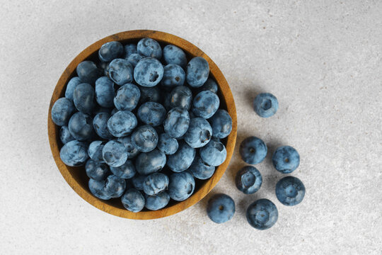 Fresh ripe blueberries in wooden bowl on a light gray textured background. Seasonal summer harvest, healthy food, natural nutrition, wholesome eating and nutritious source of vitamins and antioxidants