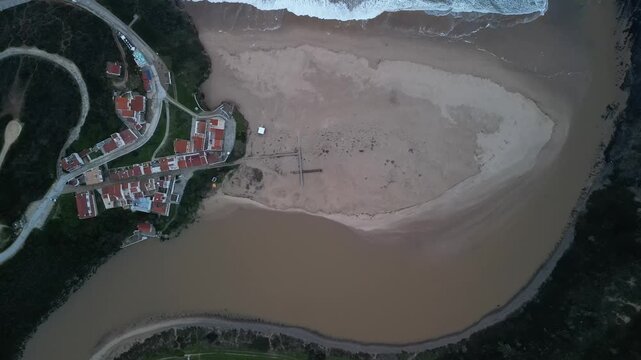 Aerial view of Odeceixe beach and river mouth with sandy shores and nearby village buildings in Odeceixe, Faro District, Portugal.