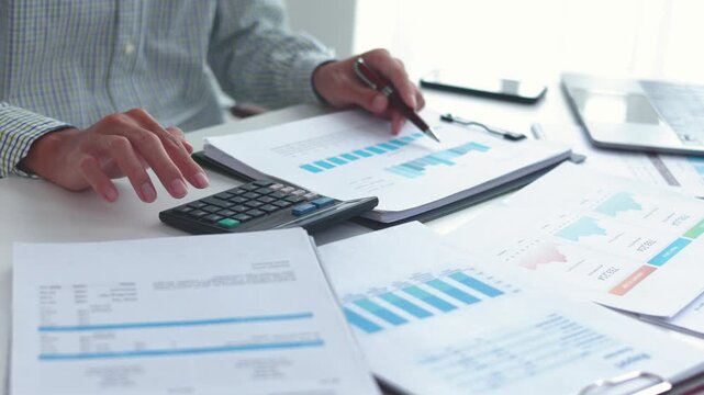 Businessman working at office desk using calculator analyzing financial charts data in office.