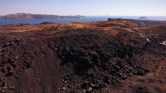 Breathtaking drone aerial video of the Tholos Naftilos volcanic dome on Nea Kameni, showcasing the dark barren lava rocks against the deep blue Aegean Sea, Santorini, Greece.