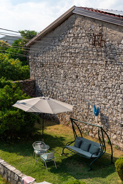 Podgorica, Montenegro - 20 June 2025: View of a garden patio featuring a swing bench and a small table set against a rustic stone wall.