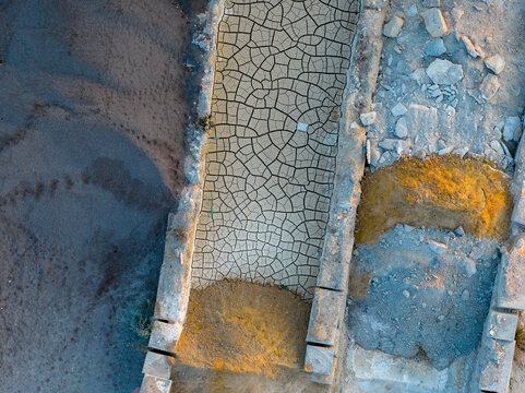 Aerial view of a dry, cracked earth path bordered by stone walls and piles of dirt in an industrial area in Rome, Lazio, Italy.