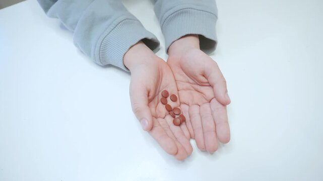 Children's hands are holding strange pills. Drug control and drug control. The child holds brown pills in his closed hands and hides them
