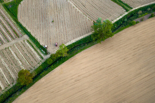 Aerial view of agricultural fields with rows of crops, a tractor working the land, and a small stream lined with trees in Piantravigne, Tuscany, Italy.