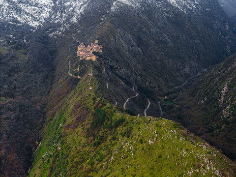 Aerial view of the historic village of Anversa degli Abruzzi perched on a narrow mountain ridge with winding roads and snow-capped peaks in Anversa degli Abruzzi, Abruzzo, Italy.