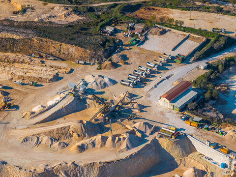Aerial view of an active quarry site with heavy machinery, parked trucks, and piles of sand and gravel in Capestrano, Abruzzo, Italy.