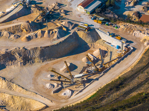 Aerial view of an active stone quarry with conveyor belts, piles of gravel and sand, and industrial machinery in Capestrano, Abruzzo, Italy.