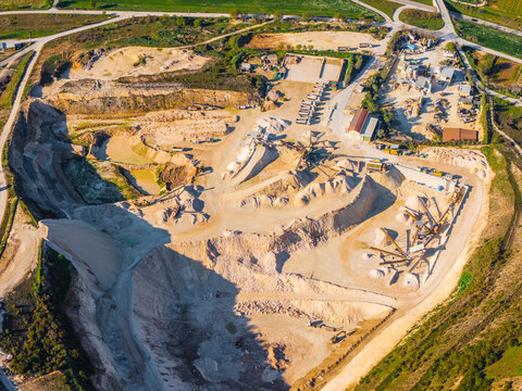 Aerial view of an active quarry with piles of gravel and sand, heavy machinery, and industrial processing equipment in the rural landscape of Capestrano, Abruzzo, Italy.