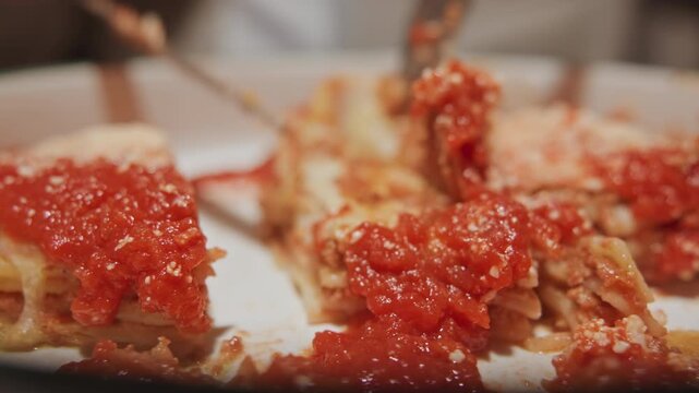 Close up of deep dish pizza slices with rich red tomato sauce and melted cheese. Fork repeatedly lifts slice revealing layers beneath vibrant topping. Soft lighting highlights texture