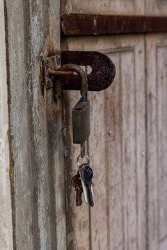 A rusty padlock and old keys hang from a weathered latch on a peeling wooden door in Valletta, Malta