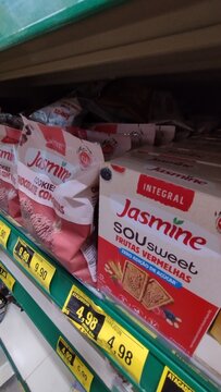 ITABIRA, BRAZIL - AUGUST 26, 2026: Packages and boxes of Jasmine whole grain cookies with zero added sugar displayed on a supermarket shelf above retail price tags.