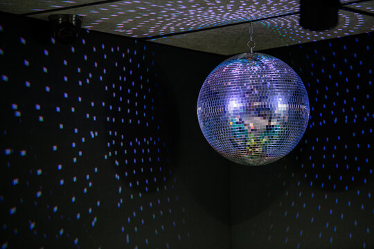 Shiny disco ball hanging from ceiling in dark room with colorful light reflections on walls. Night club party decoration with spotlight. Music dance entertainment celebration