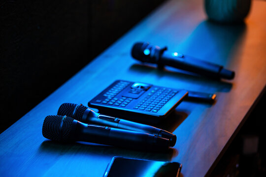Wireless microphones and mini keyboard on wooden table in blue neon light. Audio equipment for conference, presentation and karaoke. Sound recording and event technology concept