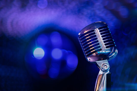 Retro microphone on stage with blue neon lights and smoke. Vintage microphone closeup on concert background with bokeh. Music, singing, karaoke and entertainment concept.