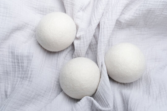 Wool laundry dryer balls arranged on a textured white fabric background, showcasing their round shape and soft texture for effective laundry care solutions