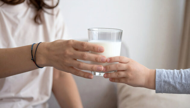Glass of milk being passed from a mother to her young child in a bright home living room setting