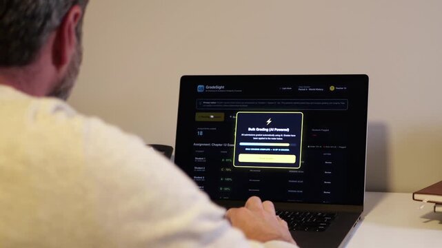 Educator at a laptop using AI software for automated bulk grading of student essays while scanning for unauthorized student AI usage and plagiarism