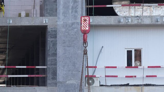 Crane hook and lifting equipment suspended beside a high rise building under construction, representing heavy lifting, rigging operations and construction site logistics