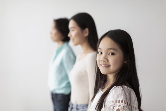 Smiling Asian Girl Standing In Bright Indoor Setting With Mother And Older Woman, Showing Family Bonding. Joyful Family Togetherness And Connection In A Modern Indoor Environment.