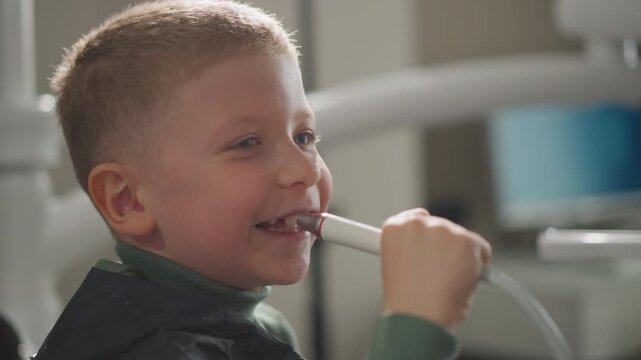 Close up of young boy holding dental tool in orthodontic clinic wearing green turtleneck and black cape. Dental equipment visible with soft lighting and calm expression. Indoor setting