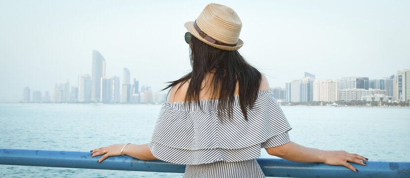 Woman tourist on viewpoint admire picturesque sunset and turquoise waterfront with scenic Abu dhabi metropolis skyline background. Traveler enjoy holidays visit sightseeing explore emirates capital
