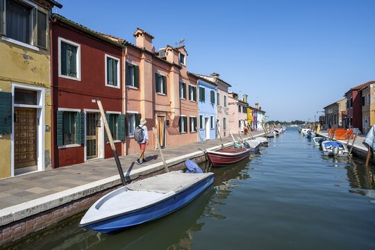 Young man in front of colourful houses on the canal, canal with boats and colourful house facades, Burano Island, Venice, Veneto, Italy
