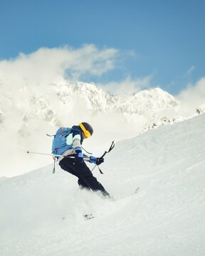 Cool skier performing switch skiing trick backwards on snowy slope with mountains in background