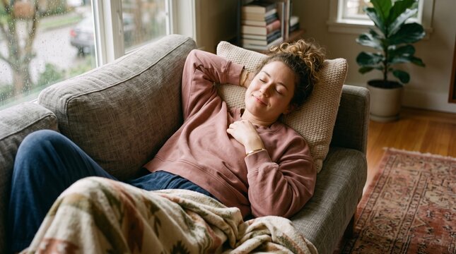 Woman resting on a sofa by a rainy window