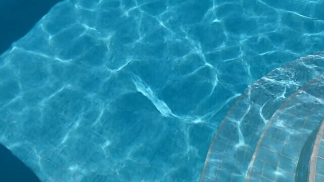 clear blue swimming pool water with sunlight caustics reflection on tiled pool steps
