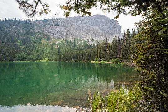 Lillian Lake calm summer waters reflecting surrounding coniferous forest and rocky peaks. Kananaskis, Alberta, Canada.
