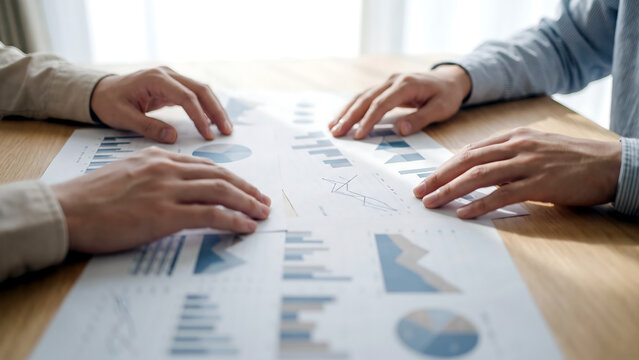 折れ線と棒のグラフが重なる紙束の俯瞰に見る業績の分析と検討の場面