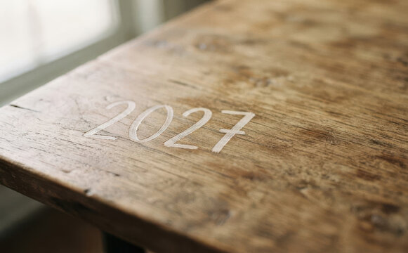 Year 2027 carved into a rustic wooden table surface representing future planning, time, and milestones