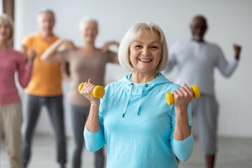 Smiling Senior Woman Holding Dumbbells While Exercising With Group Of Senior Friends, Engaging In...