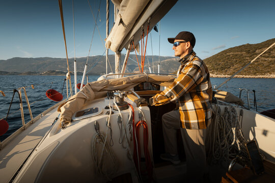 Young male captain standing at the helm of a sailing yacht and looking into the distance