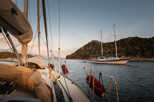View from sailing yacht crossing paths with another sailboat at sunset near islands