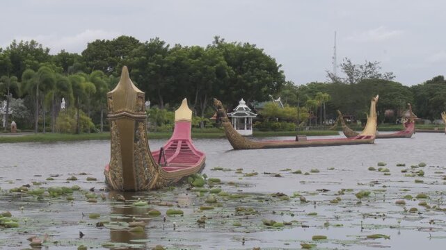 ornate thai royal barges floating on a calm pond covered with water lily pads surrounded by lush green trees