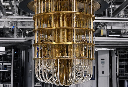 Golden quantum computer dilution refrigerator core suspended from ceiling resembling chandelier in physics lab