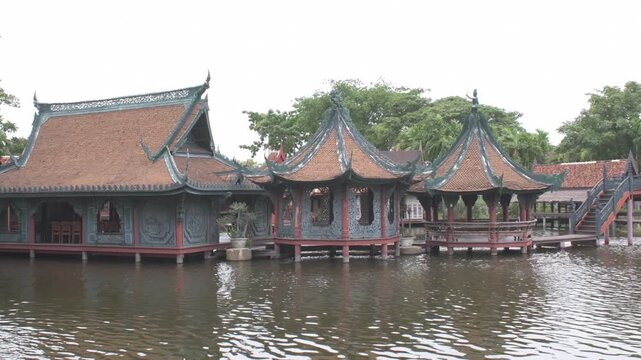 traditional wooden floating market pavilions on stilts and arched walkway bridge over calm canal water, thailand