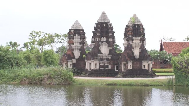 three historic khmer style stone prangs standing beside a calm lake with water reflections and lush green trees