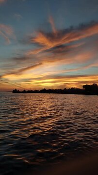 Vertical medium shot of vibrant orange twilight sky glowing over coastal waters with dark ocean ripples reflecting the warm sunset light in Biak Island for travel documentaries and commercial B-roll.