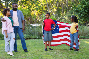 Obraz premium African American family of two boys standing on yard holding large US flag in casual clothes
