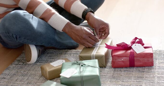 Hands are reaching, selecting gold-wrapped box on patterned rug and writing name tag for gifting
