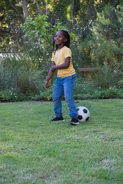 Female child standing smiling on grass lawn wearing yellow shirt and blue jeans with soccer ball