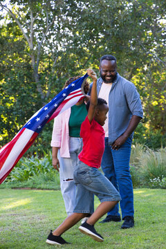 African American family smiling and watching schoolboy running with large American flag on lawn