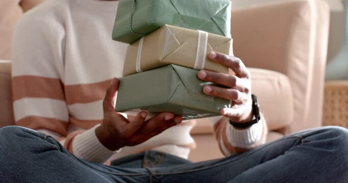 Balancing gifts, man in cream sweater and hat adjusting stacked gifts on couch to steady boxes