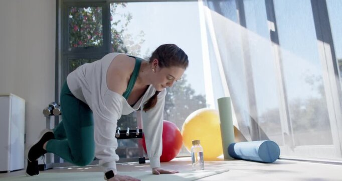 Woman starting forearm plank alternating knee drives on mat by water bottle at home building core