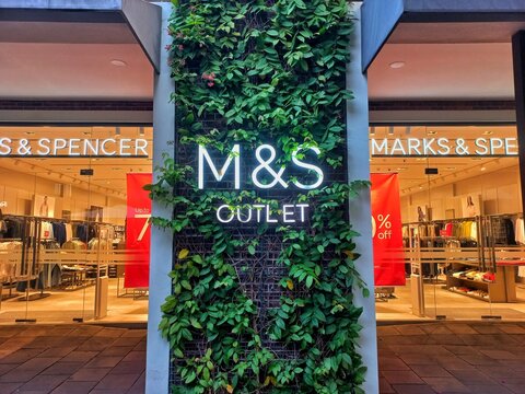 Karawang, Indonesia - August 11, 2026: Marks & Spencer Outlet storefront featuring an illuminated brand logo on a green vertical garden wall at Summarecon Villaggio Outlets.