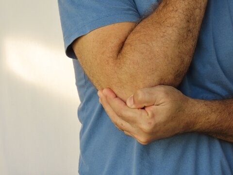 Closeup of man in blue cotton t-shirt holding his elbow in pain. Body pain concept.